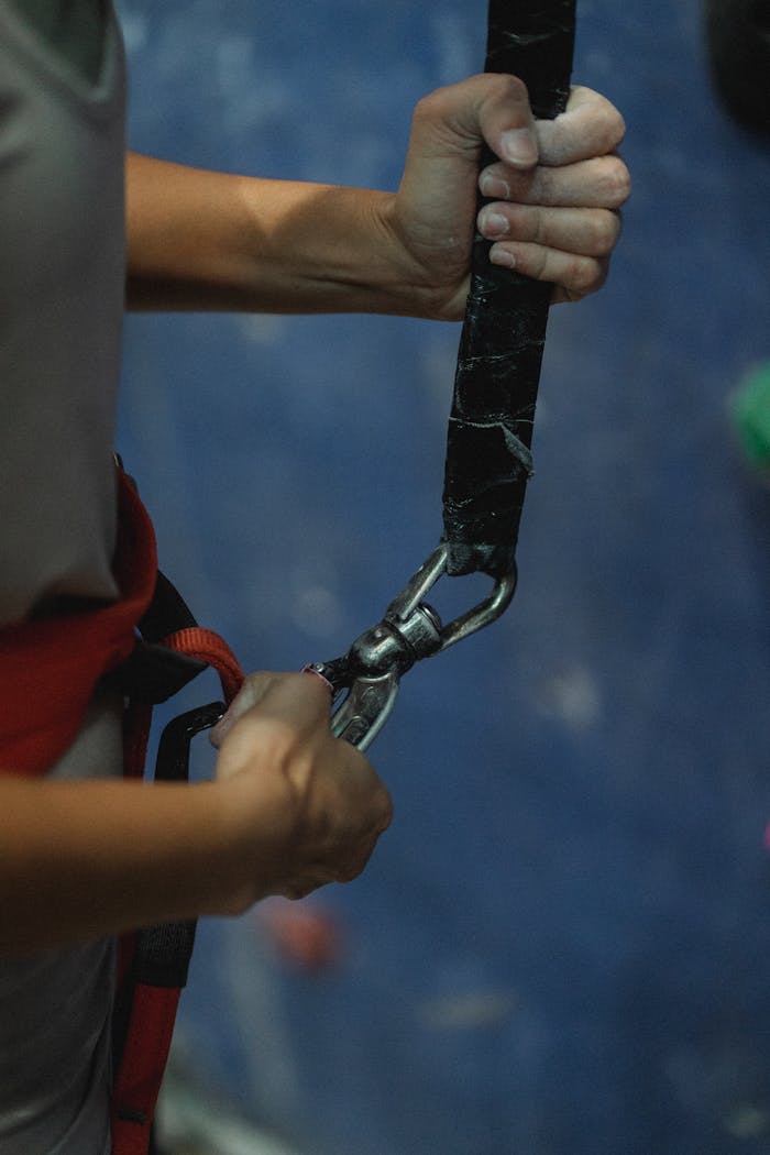 Side view of crop anonymous fit female alpinist with harness preparing to practice extreme sport near climbing wall